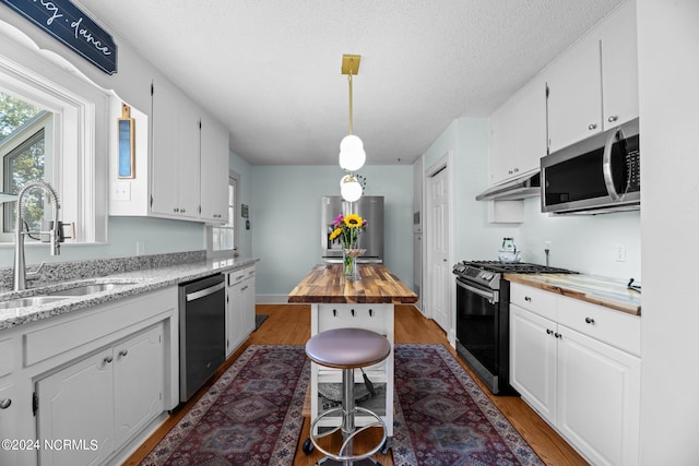 kitchen featuring white cabinets, butcher block counters, hanging light fixtures, appliances with stainless steel finishes, and hardwood / wood-style floors