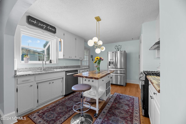 kitchen with appliances with stainless steel finishes, butcher block countertops, sink, and white cabinets