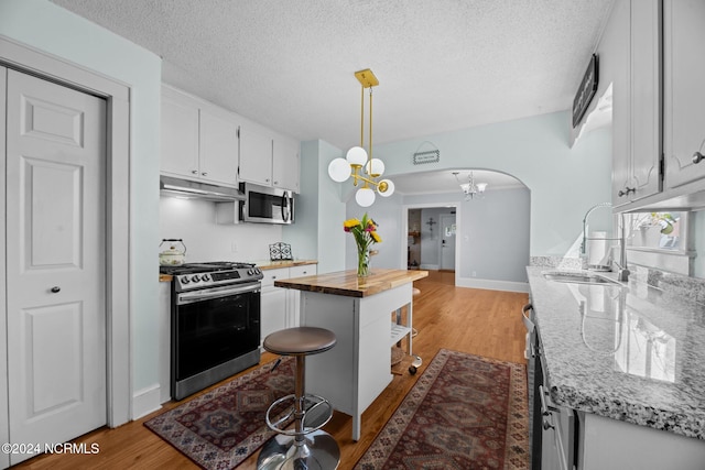 kitchen featuring white cabinets, butcher block counters, pendant lighting, stainless steel appliances, and light wood-type flooring