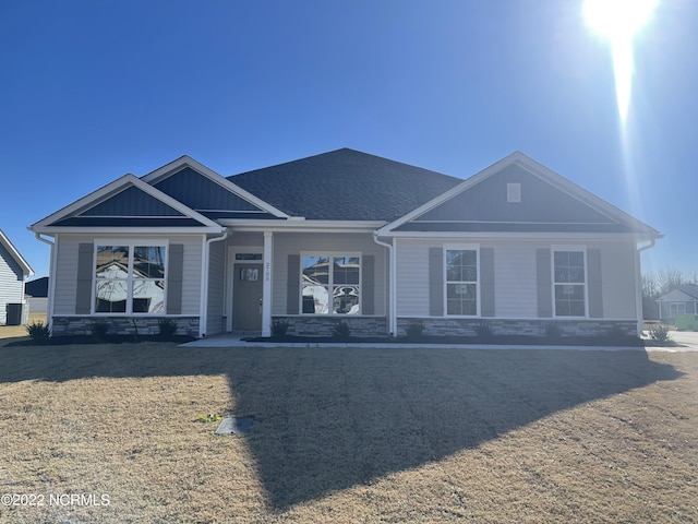 view of front of home with a porch, board and batten siding, a front yard, and stone siding