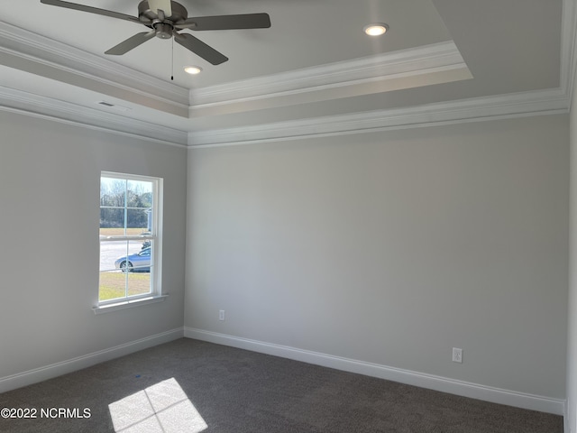 empty room with dark carpet, a tray ceiling, ornamental molding, and ceiling fan