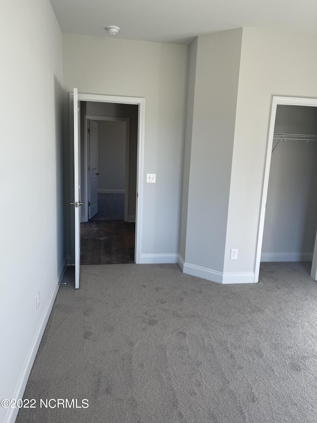 unfurnished bedroom with dark colored carpet and a closet