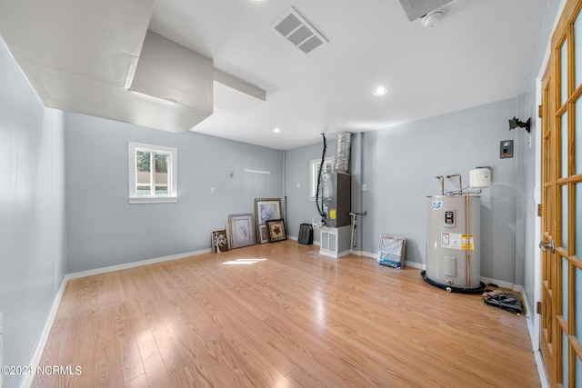 misc room with heating unit, light wood-type flooring, and electric water heater