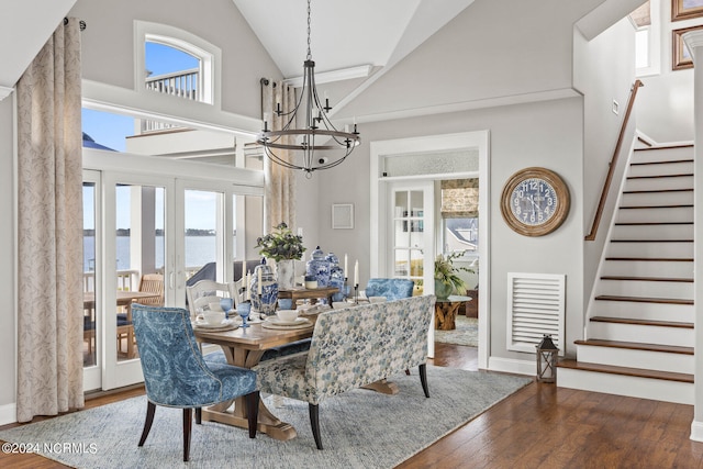 dining area with french doors, a chandelier, high vaulted ceiling, dark hardwood / wood-style floors, and a water view