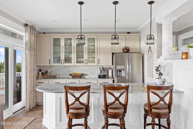 kitchen with ornate columns, tasteful backsplash, stainless steel refrigerator with ice dispenser, light stone countertops, and a kitchen bar