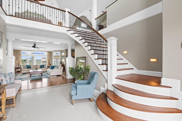 stairway with ceiling fan, a towering ceiling, and decorative columns