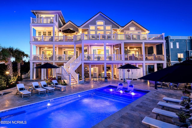 back house at dusk with a balcony, a patio area, and a pool with hot tub