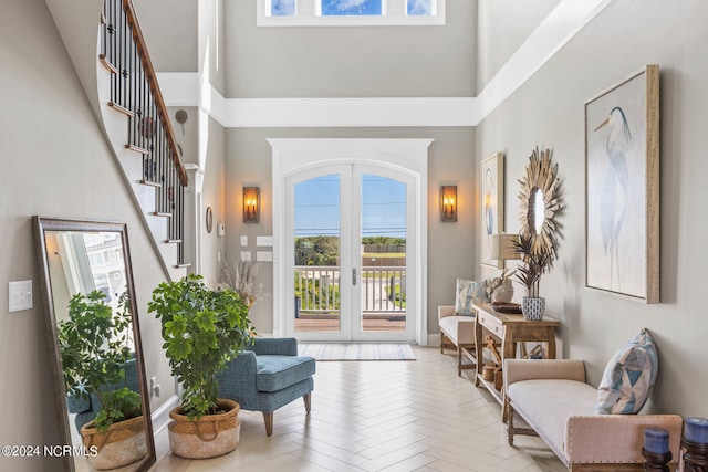 foyer entrance with light parquet flooring, a high ceiling, and french doors