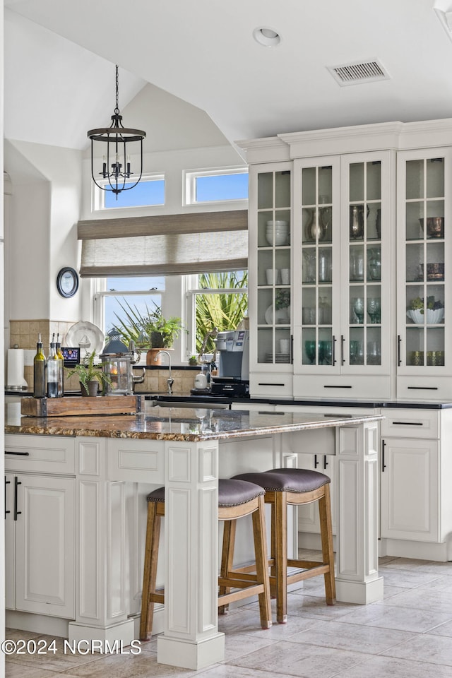 kitchen featuring dark stone countertops, vaulted ceiling, white cabinets, backsplash, and a breakfast bar area