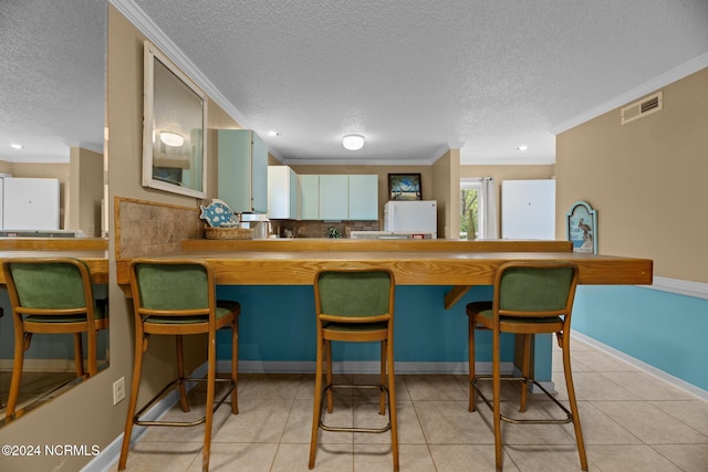 kitchen with ornamental molding, light tile patterned flooring, kitchen peninsula, and a textured ceiling