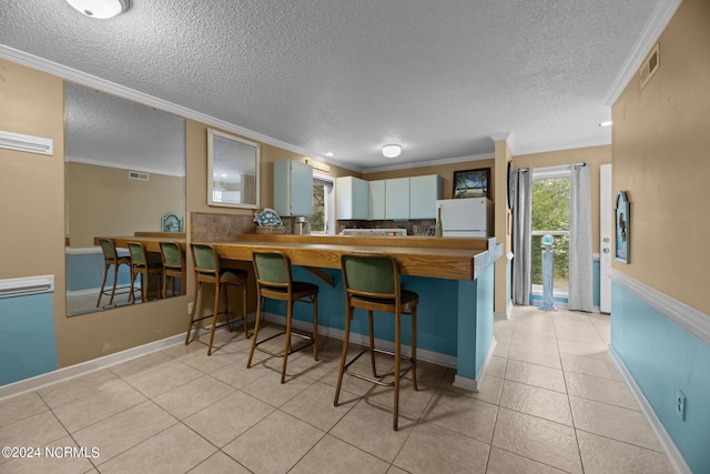 kitchen featuring kitchen peninsula, crown molding, light tile patterned flooring, white fridge, and a textured ceiling