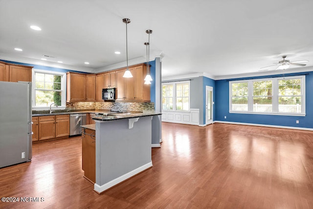 kitchen featuring hanging light fixtures, sink, dark stone countertops, appliances with stainless steel finishes, and a breakfast bar area