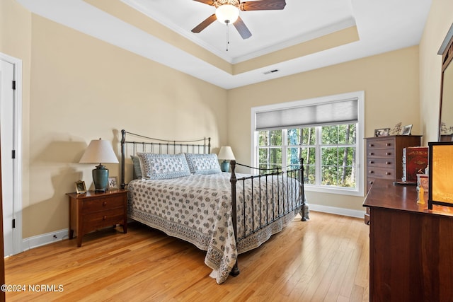 bedroom with ceiling fan, light wood-type flooring, crown molding, and a raised ceiling