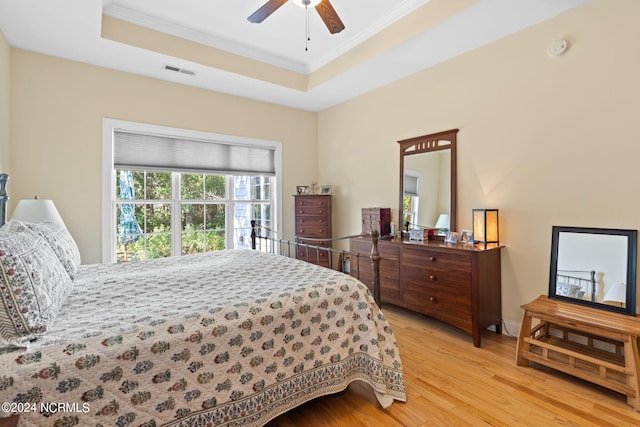 bedroom featuring ceiling fan, ornamental molding, a tray ceiling, and light hardwood / wood-style floors