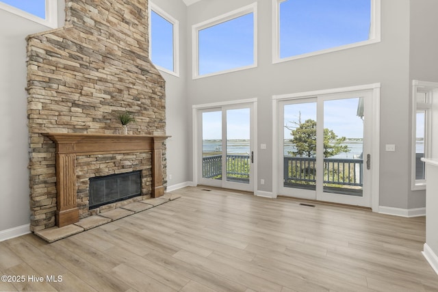 10002 Coast Guard Rd, Emerald Isle, NC 28594 - unfurnished living room with a towering ceiling, a stone fireplace, wood finished floors, baseboards, and a water view