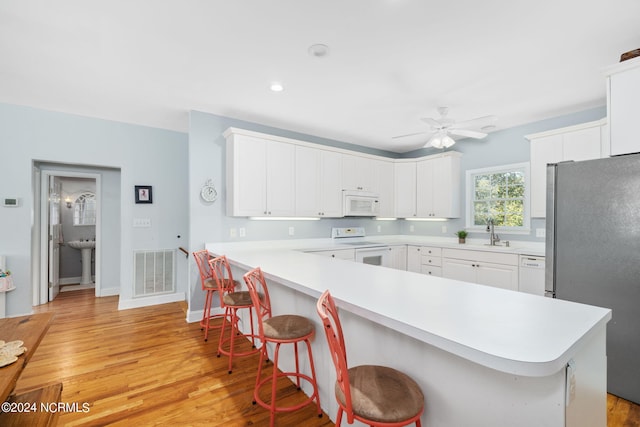 kitchen featuring white cabinetry, white appliances, a breakfast bar, and light hardwood / wood-style flooring