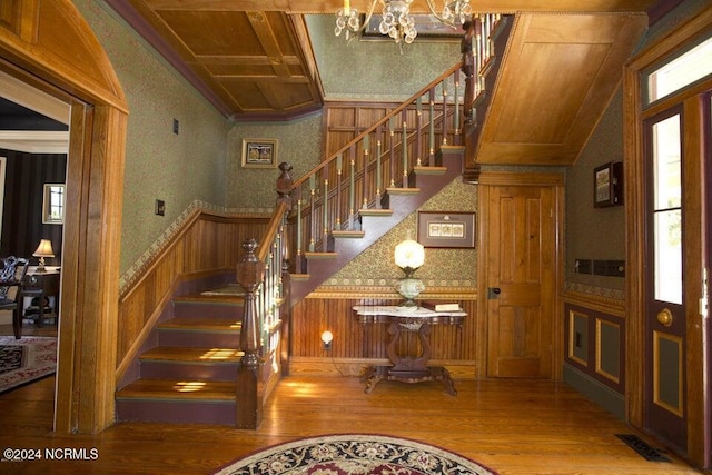 stairs with hardwood / wood-style flooring, an inviting chandelier, crown molding, and wood walls