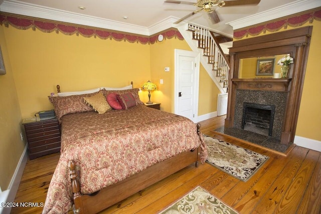 bedroom featuring a fireplace, hardwood / wood-style floors, ceiling fan, and ornamental molding