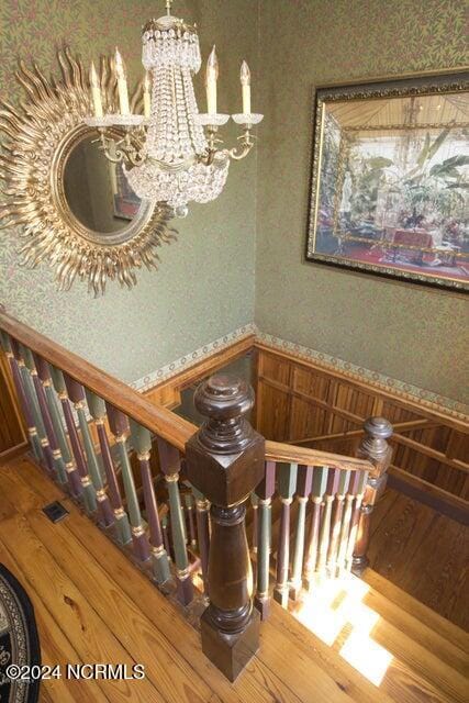 stairs featuring wood-type flooring, a notable chandelier, and wood walls