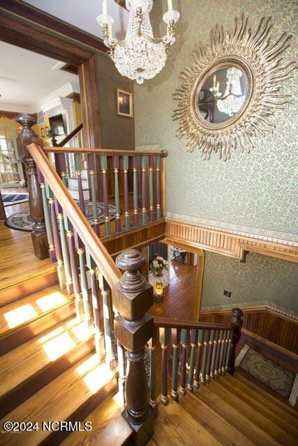 staircase featuring crown molding, an inviting chandelier, and hardwood / wood-style flooring