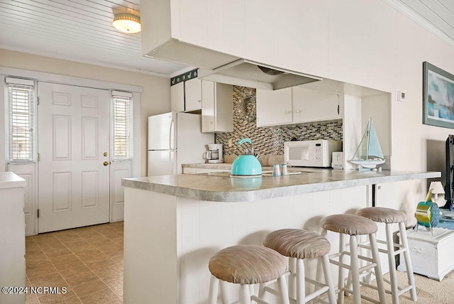 kitchen featuring white appliances, white cabinetry, decorative backsplash, and a breakfast bar