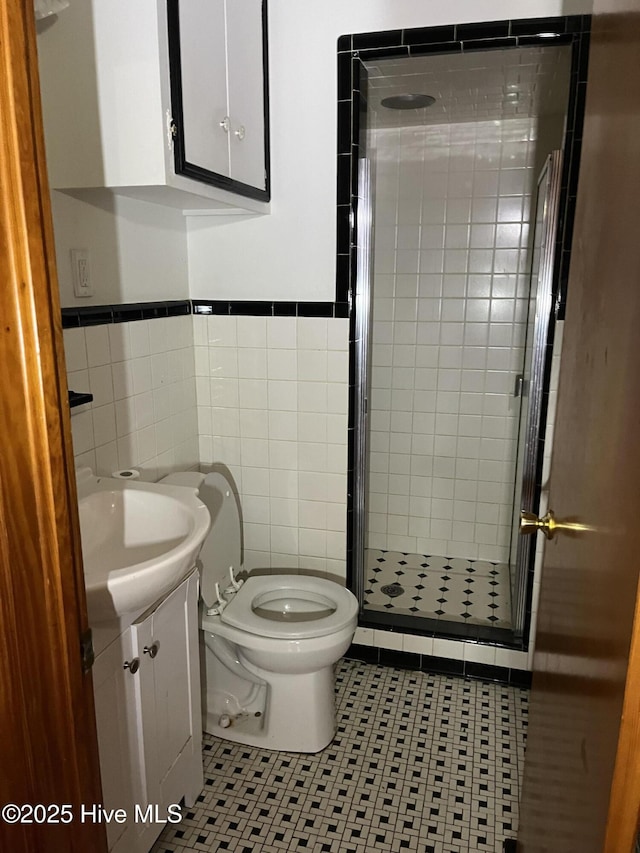 bathroom featuring tile patterned floors, vanity, tile walls, toilet, and a shower with shower door