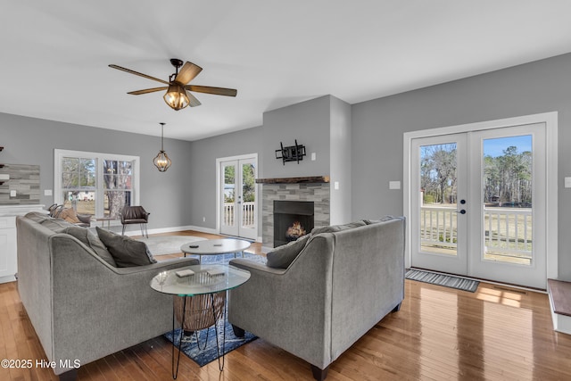 living room with a stone fireplace, french doors, wood-type flooring, and baseboards