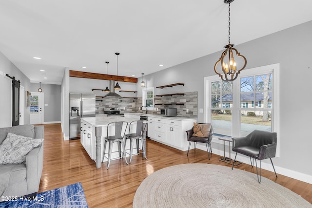 kitchen with open shelves, decorative backsplash, a barn door, appliances with stainless steel finishes, and white cabinetry