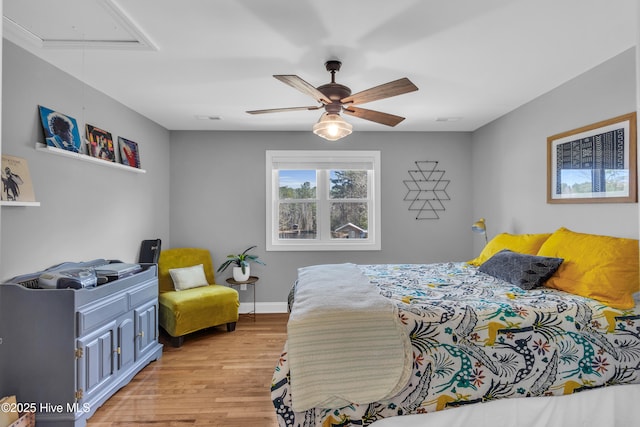 bedroom featuring light wood-style floors, attic access, visible vents, and a ceiling fan