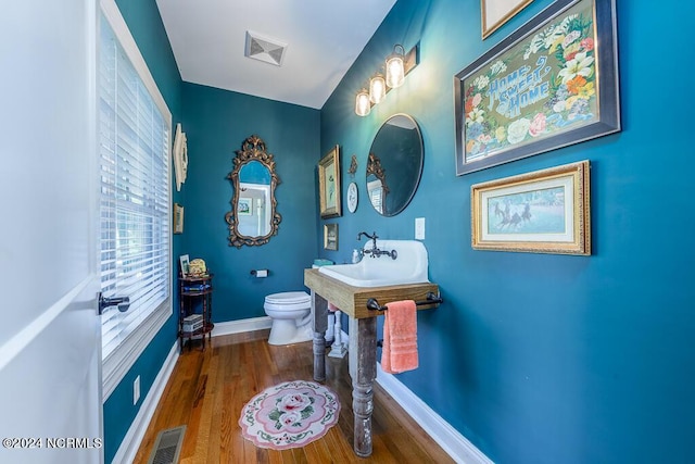 bathroom with toilet, wood finished floors, visible vents, a sink, and baseboards