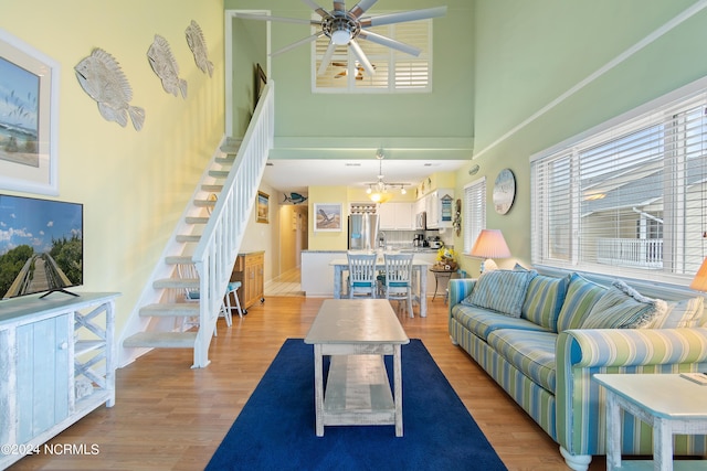 living room featuring a high ceiling, ceiling fan with notable chandelier, and light hardwood / wood-style floors