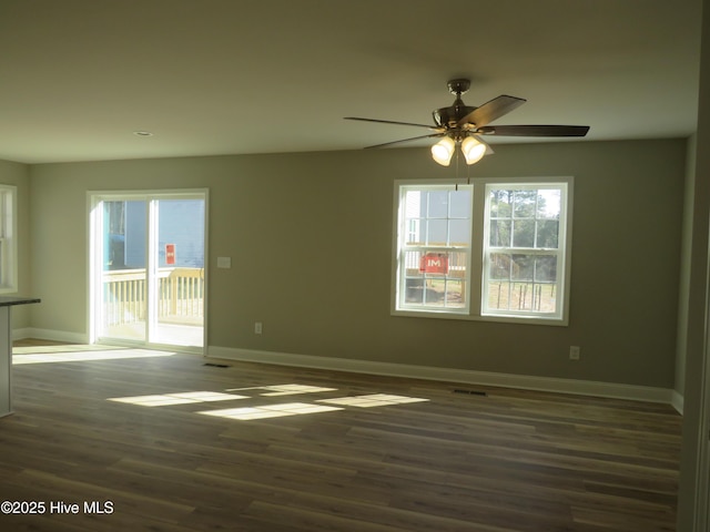 empty room with ceiling fan, dark hardwood / wood-style floors, and a healthy amount of sunlight