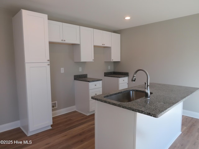 kitchen featuring sink, wood-type flooring, white cabinets, and an island with sink