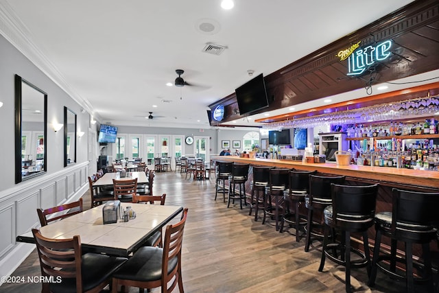 dining space featuring bar area, wood-type flooring, ceiling fan, and crown molding