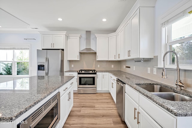 kitchen featuring white cabinetry, sink, wall chimney exhaust hood, light hardwood / wood-style floors, and appliances with stainless steel finishes