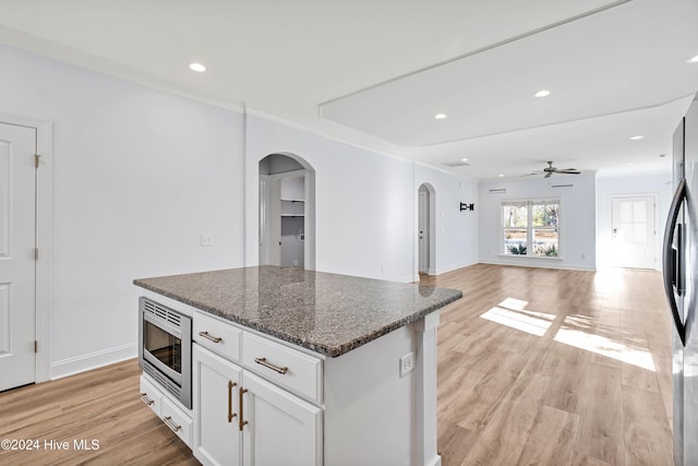 kitchen with white cabinets, a kitchen island, stainless steel microwave, and light hardwood / wood-style flooring