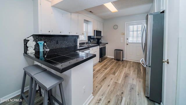 kitchen with stainless steel appliances, a peninsula, white cabinets, light wood finished floors, and a healthy amount of sunlight