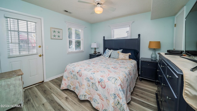 bedroom featuring visible vents, baseboards, ceiling fan, light wood-style floors, and a textured ceiling