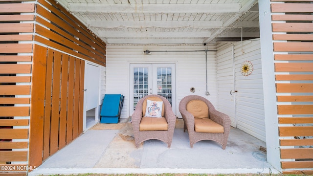 sitting room featuring beam ceiling, wooden walls, french doors, and concrete flooring