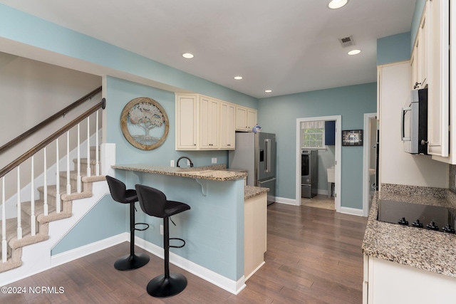 kitchen with a kitchen breakfast bar, washer / clothes dryer, stainless steel appliances, light stone countertops, and dark wood-type flooring