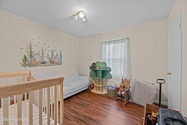 bedroom with a textured ceiling, hardwood / wood-style flooring, and a crib