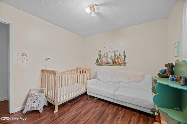 bedroom with a nursery area, dark wood-type flooring, and a textured ceiling