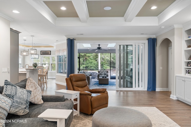 living room with ceiling fan with notable chandelier, ornamental molding, light hardwood / wood-style flooring, and a raised ceiling