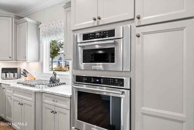 kitchen featuring white cabinetry, light stone counters, tasteful backsplash, stainless steel appliances, and crown molding