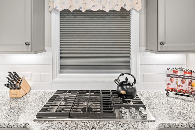 room details featuring gas cooktop, gray cabinetry, decorative backsplash, and light stone counters