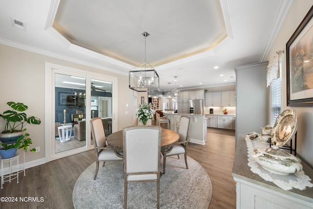 dining space featuring hardwood / wood-style flooring, a raised ceiling, crown molding, and a notable chandelier