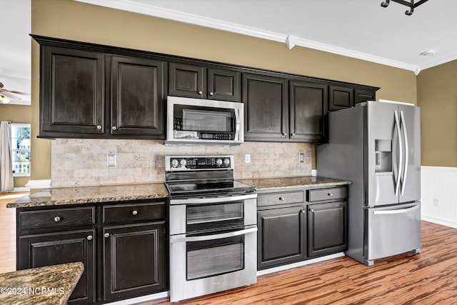 kitchen featuring light wood-type flooring, stainless steel appliances, dark stone counters, and crown molding