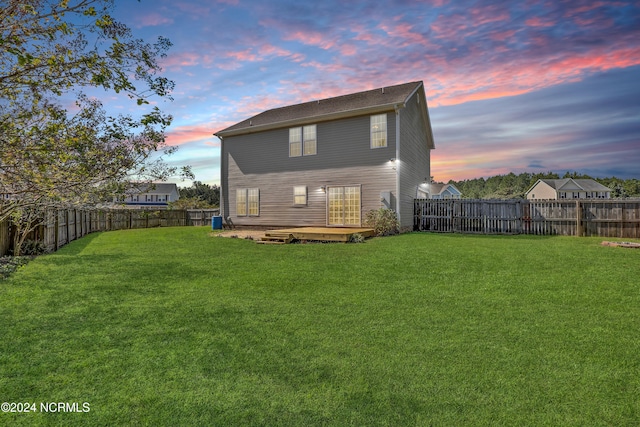 back house at dusk with a yard and a wooden deck