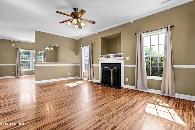 unfurnished living room with ceiling fan, a healthy amount of sunlight, light wood-type flooring, and crown molding