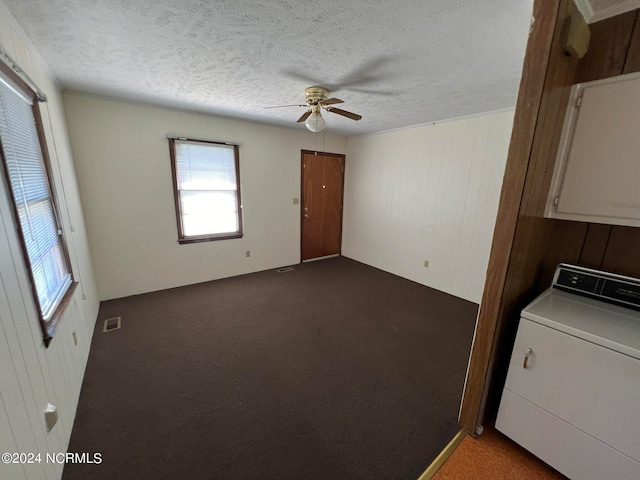 carpeted spare room with a textured ceiling, washer / clothes dryer, wooden walls, and ceiling fan